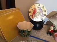 Photo showing four yellow chair cushions stacked with a cream flower-shaped pot and outdoor thermometer with bird motif