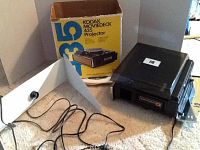 Photo of Kodak Moviedeck 435 projector unit next to its original box and power cable, displayed on carpet.