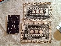 Two painted woven basket mats and one painted rectangular mat with black and white tribal geometric patterns.