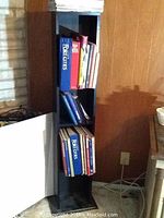 Black 3-shelf bookcase filled with assorted books and magazines, showing the contents and structure of the bookcase.