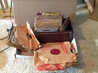 Box with assorted record albums and vintage 45 rpm discs with well-worn sleeves.