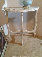 Distressed white demilune table with visible damage on the top.