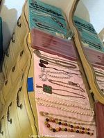 Photo of assorted costume jewelry pieces including necklaces and bracelets displayed on two jewelry trays placed on a cream-colored dresser with drawers.