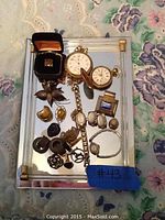 Wide view of assorted vintage jewelry and three pocket watches on mirror tray.