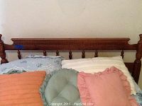 Close-up image of the wooden headboard showing carved details and spindles with some cushions and pillows resting against it.