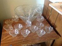 Glass punch bowl with 12 matching cups and ladle arranged on a wooden table, all items displaying clear cut glass starburst pattern.