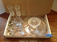 View of the assorted crystal glass pieces arranged in a box on a wooden surface, showing the variety of dishware included, with a blue tape marked '#60'.