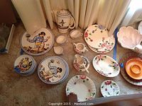 Indian china plates, cups, creamer, and teapot with Indigenous tribal warrior designs. Blue Ridge hand-painted floral dish set also shown, both sets on a floor.
