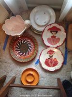 Overview of assorted plates including decorative plates, patterned plate, seashell bowl, chip and dip dish, and plain plates stacked.