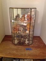 Full shot of glass curio display case on wooden table showing the shelves and contents inside including multiple figurines.