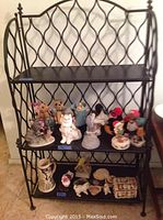 Front view of the black metal bookcase showing three shelves and decorative curved metal sides. The shelves hold various decorative items.