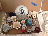 Photo showing assorted candlestick holders, decorative glass and ceramic pieces, including a decorative plate, animal-shaped items, and small pitchers.