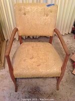 Front view of the vintage occasional chair showing upholstered firm seat and tufted backrest with visible stains and wooden armrests.