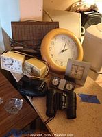Photo showing multiple clocks including wall clock, smaller clocks, a clock radio, compact binoculars, and a small glass dish on a countertop.