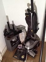 Kirby G6 Micron Magic vacuum with attachments stored on attachment holder, extra bags, and operator's manuals on floor beside it, shot in a corner against white walls