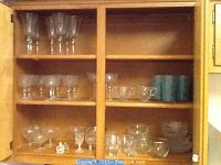 Wide view of wooden cabinet holding multiple shelves of glassware including clear stemware, bowls, and tumblers.