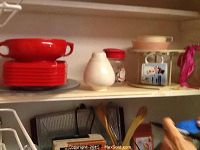 View of red plates and bowls stacked on shelf alongside white ceramic container and vintage appliances including the Oster massage instrument and hand crank ice crusher.