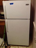 White Frigidaire refrigerator showing entire front with top freezer and bottom refrigerator doors, positioned between a counter and a wall.