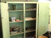 Full view of the green metal outdoor storage cabinet with three doors open revealing three shelves holding assorted yard items and tools.