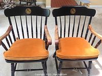 Two black-painted Windsor-style armchairs with gold seat cushions and university seal backrests.
