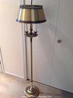 Full view of the tall brass floor lamp showing height, base, pole, light sockets and metal shade.