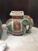 Close-up of one ceramic elephant base with intricate decorative details and square platform for supporting glass top.