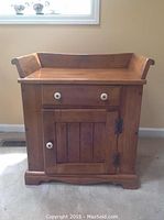 Front view of wood washstand showing drawer and cabinet door with white knobs and dark metal hinges.