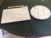 Photo of rectangular marble pastry board and round marble lazy Susan on a dark surface.
