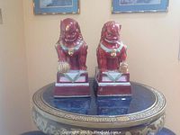 Photo showing two ceramic Foo dogs with reddish-brown glaze, turquoise collar accents, sitting on rectangular pedestals with green and white triangular decor