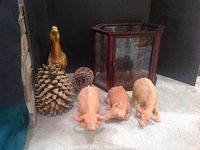 Photo showing a yellow ceramic horse figurine, three ceramic oxen pieces with visible wear, two large pinecones, and a hexagonal wooden glass display case