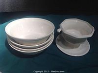 Photo showing four white bowls stacked together next to one white serving bowl with a pedestal base and scalloped edge.