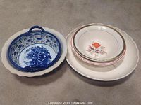 Set of various bowls on beige cloth, showing a ceramic blue and white basket bowl and several round floral decorated bowls stacked inside a larger bowl.