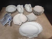 Various white ceramic serving dishes including two swan-shaped dishes, seven Japanese soup spoons with blue detail, six shell-shaped plates, two shell-shaped serving dishes, and four small square plates.