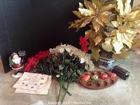 Photo of holiday decorations lot including a Santa candle holder, linen napkins, poinsettia artificial flowers in red and white, a wooden egg holder with painted eggs, a toy train, and a gold poinsettia in a ceramic pot.