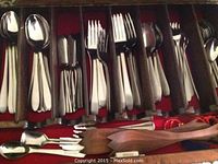 Top view of multiple stainless steel knives, forks, spoons, dessert forks and serving utensils organized in a drawer with red felt lining.