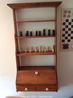Full view of the O'Hearn hanging wall desk showing four shelves, slant-front writing surface, and two drawers. Chess pieces are displayed on shelves.