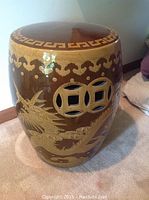 Ceramic garden stool viewed from one side showing raised dragon motif and coin-shaped cutouts.