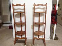 Photo showing a pair of wooden end tables with three circular shelves each, placed side by side against a wall.