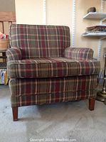 Front view of plaid upholstered armchair with cushioned seat, backrest, and armrests, wooden legs visible.