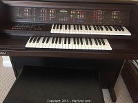 Front view of the Kawai electronic organ showing dual keyboards, various buttons and controls on the upper panel, and wood finish.