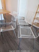 Four clear acrylic chairs grouped around a table, front angle view