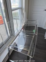 Three lucite bar stools side by side in front of window