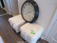 Pair of white faux fur stools with dark legs and a round wall clock behind them