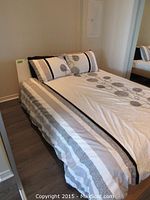 Side angle view of bed showing mattress, bedding set with white base and black floral pattern, and two matching pillows.