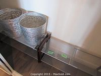 Two silver embossed tin baskets on one metal shelving unit with brown support bars.