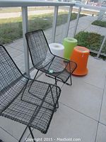 Two black woven metal chairs with grid design, seating and back, outdoors on tile floor, next to railing and three plastic stools