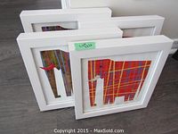 Four white framed abstract art pieces arranged angled on floor, showing colorful intersecting line patterns mostly in red, yellow, and blue.