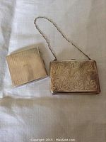 Both cases closed on fabric: left brushed cigarette case, right ornate purse case with chain