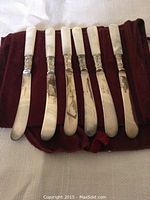 Six Birks silver plated butter knives with mother of pearl handles laid out, showing overall condition and design.
