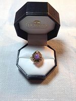 Ring displayed inside a black octagonal Howard branded jewelry box on white cushion showing front view of ring and amethyst stone.
